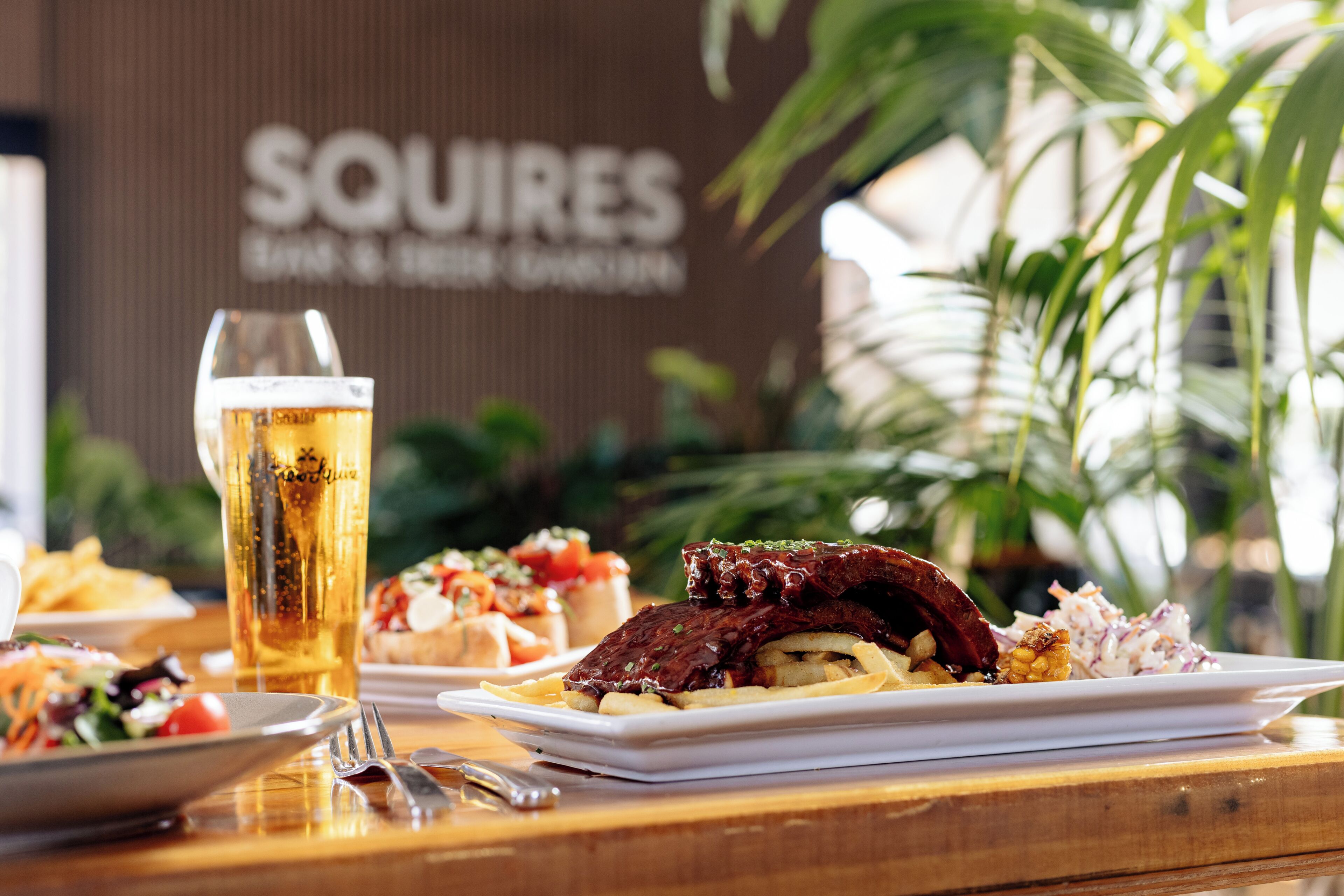 A dining table with a plate of food, a glass of beer, and a fork.
