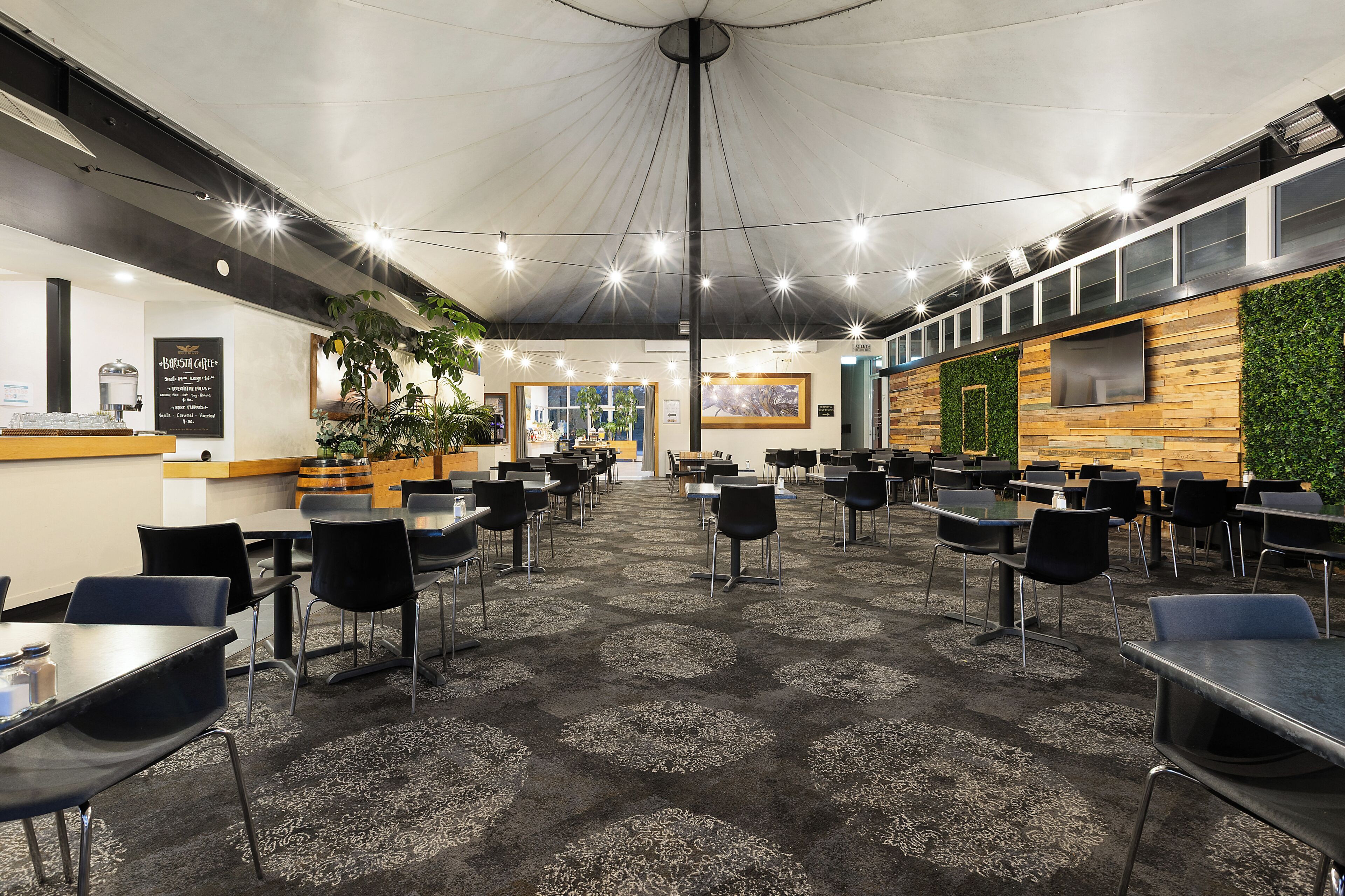 Un espacio interior amplio con mesas y sillas, una estación de café y una pared con plantas.