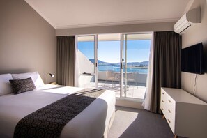 Habitación de hotel con una cama grande, un escritorio, un televisor y un balcón con vistas al mar.
