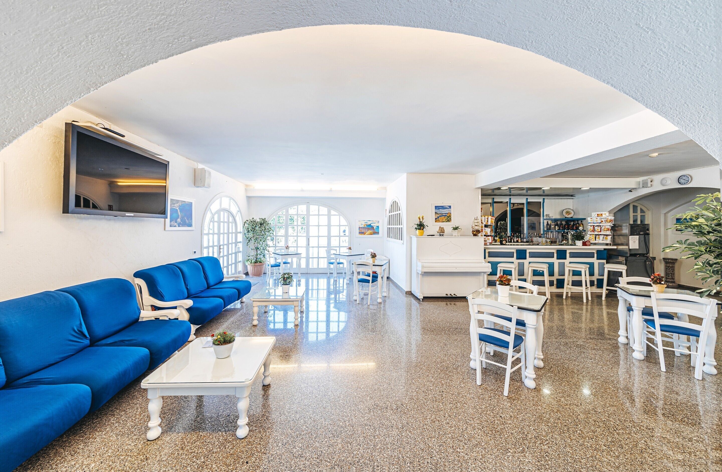 A hotel lobby with a blue sofa, white tables, and a bar area.