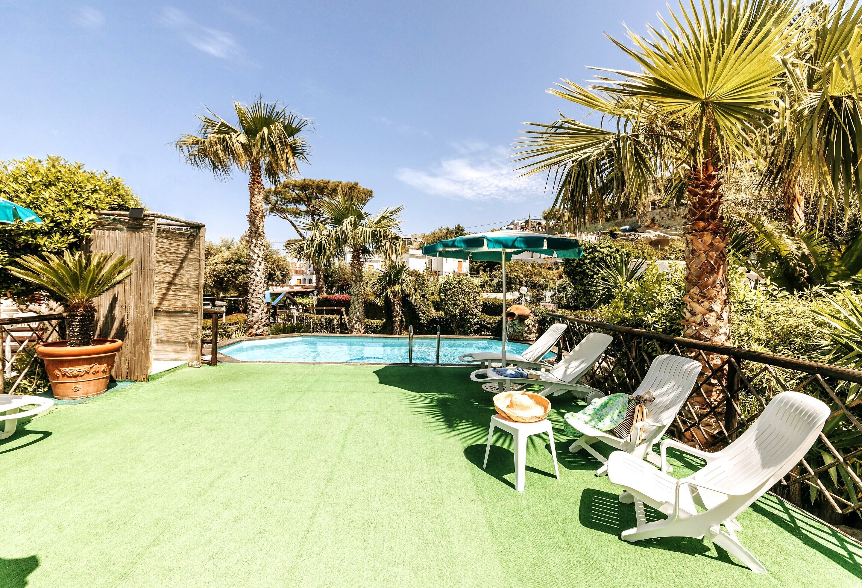 A poolside area with artificial turf, lounge chairs, and a green umbrella.