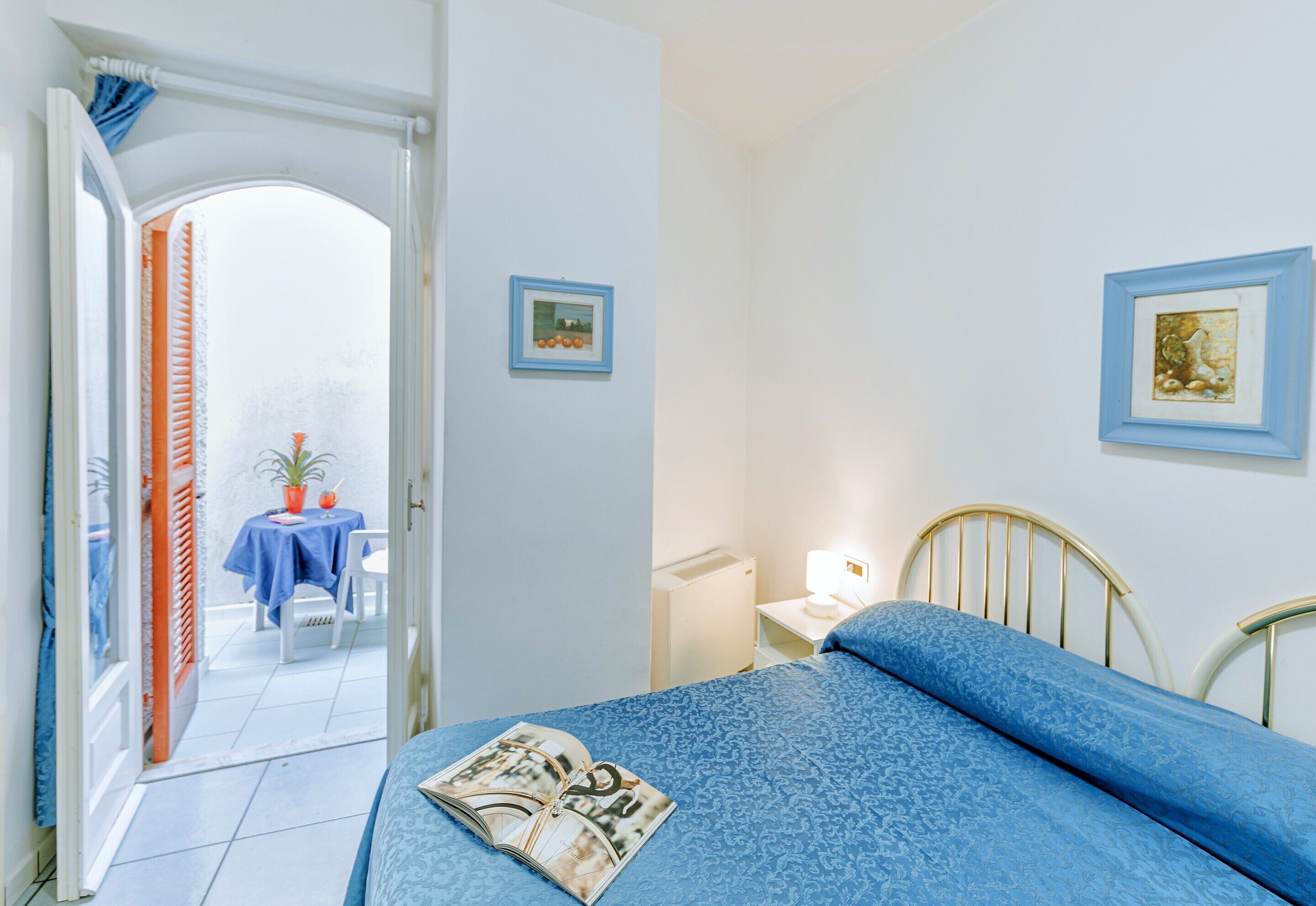 Een slaapkamer met een bed, nachtkastje, lamp en een klein tafeltje met een stoel.