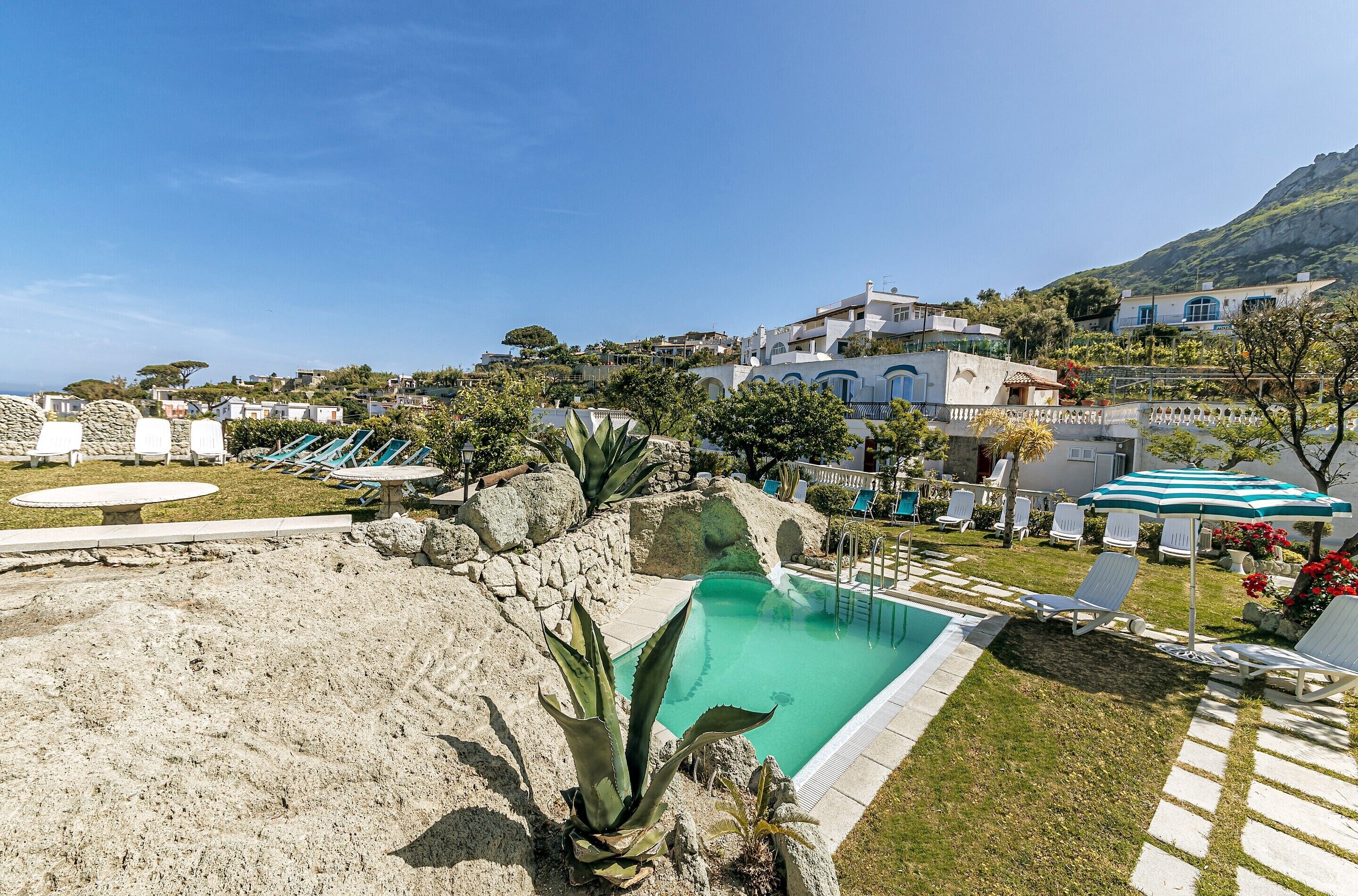 A pool area with lounge chairs, a small pool, and a view of hillside buildings.