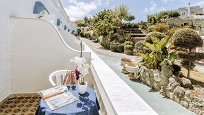 Ein Balkon mit Tisch, Blumentöpfen und Blick auf einen Garten und Gebäude.