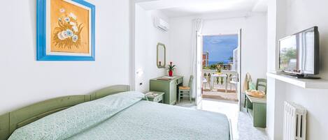 A bedroom with a bed, a desk, a chair, a television, and a view of the outside.
