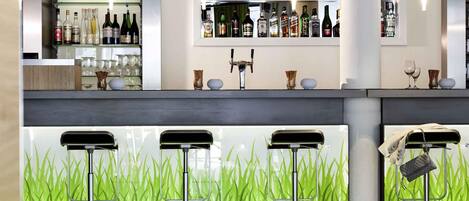 Zona de bar moderna con mostrador, estantes llenos de botellas de licor y tres taburetes.