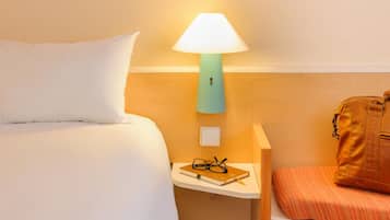 Habitación de hotel con una cama, una mesita de noche con lámpara, un par de gafas y un bolso.