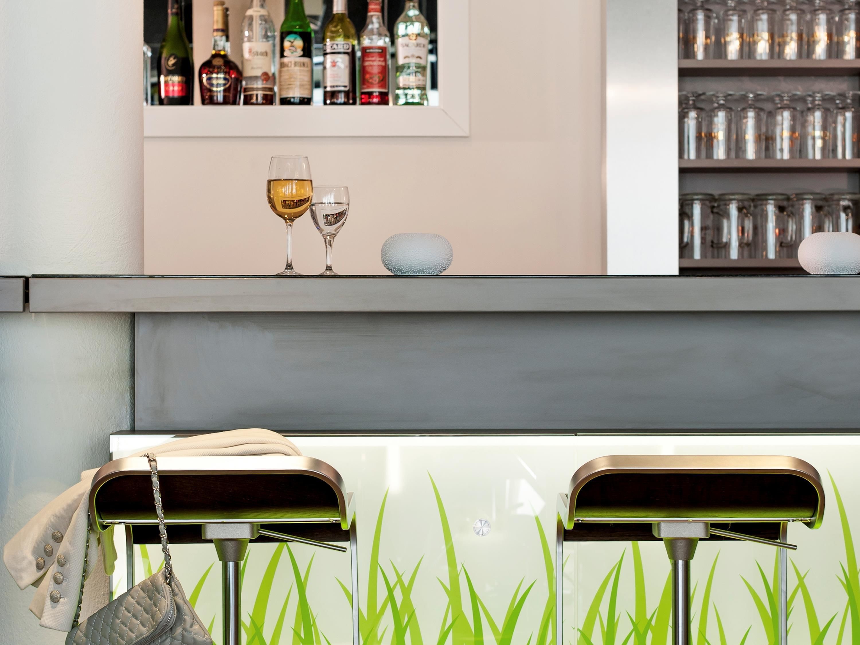 Un coin bar avec une étagère remplie de bouteilles d’alcool, deux verres et une pierre décorative.