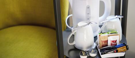 Une machine à café, une bouilloire et un plateau avec des dosettes de café et une cuillère, le tout posé sur une étagère.