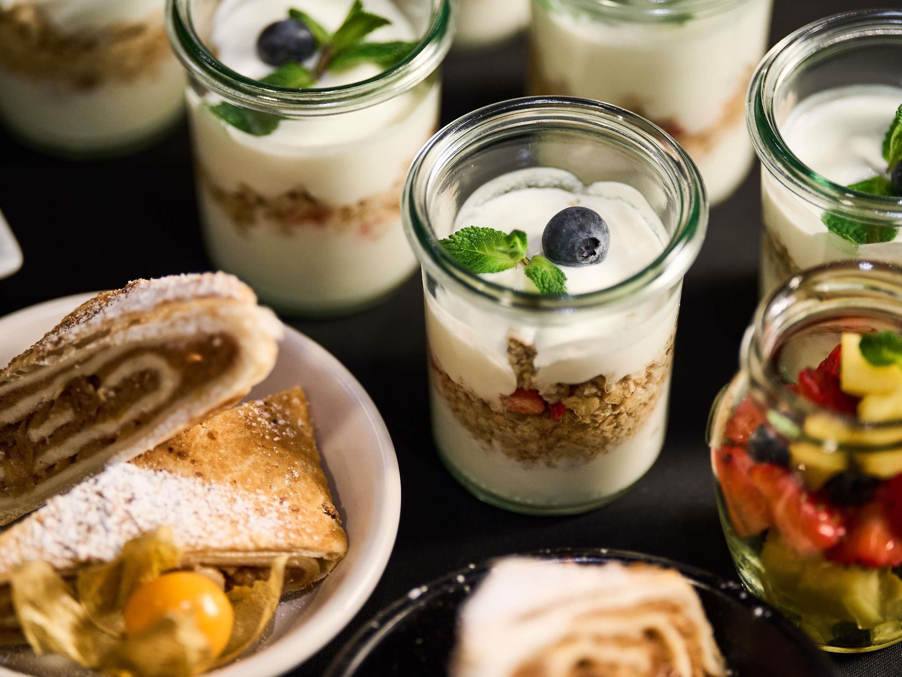 A dessert table with various pastries and a layered dessert in a jar.
