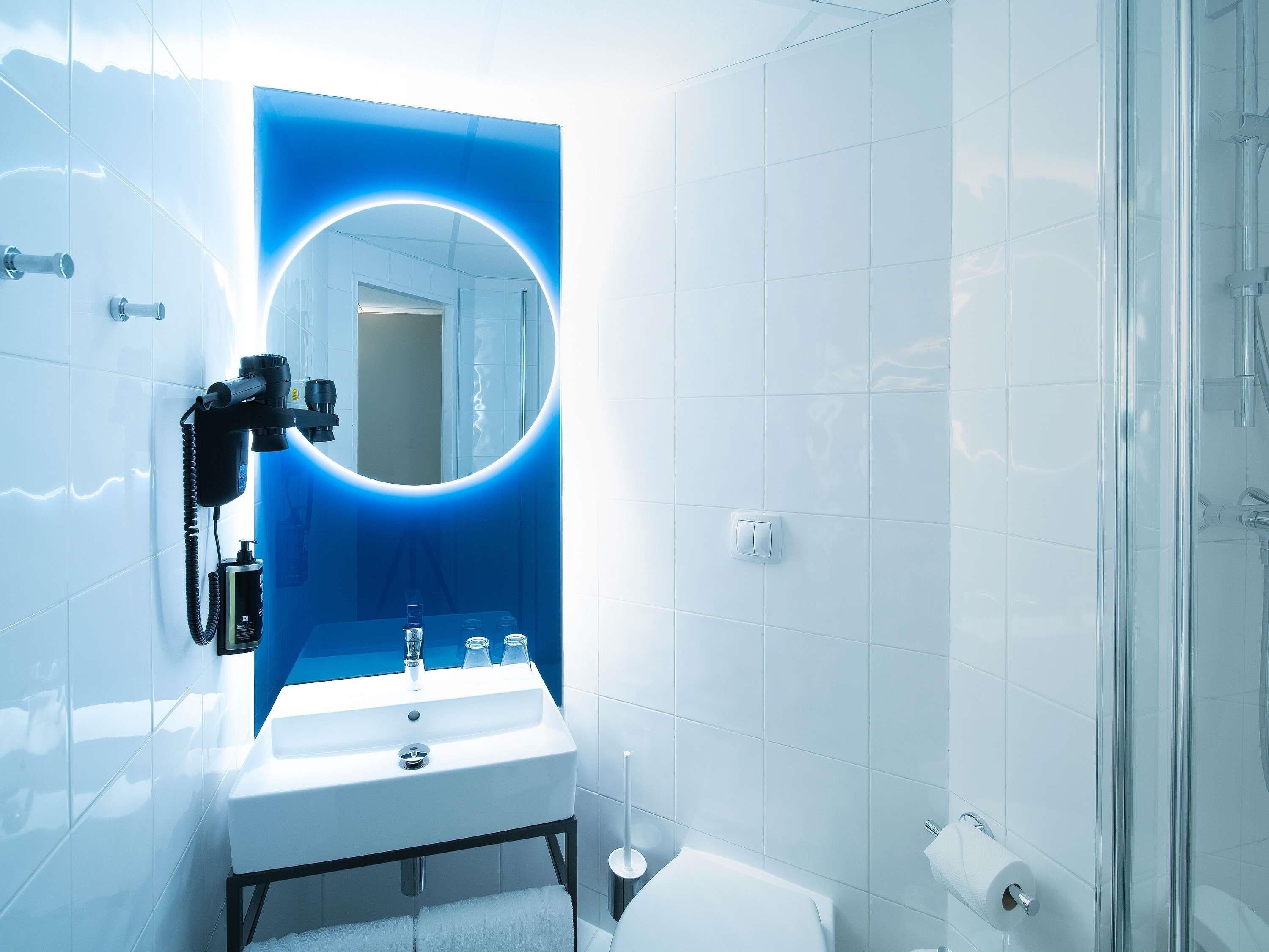 A modern bathroom with a white sink, a mirror with a blue illuminated frame, and a glass shower enclosure.