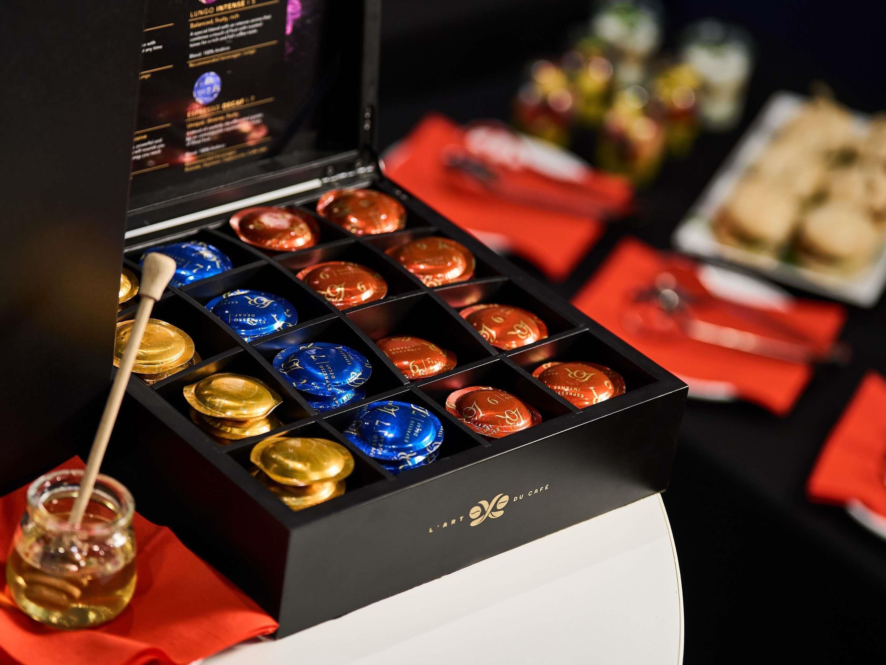 A box of assorted chocolates with a wooden spoon and honey dipper, and a menu in the background.