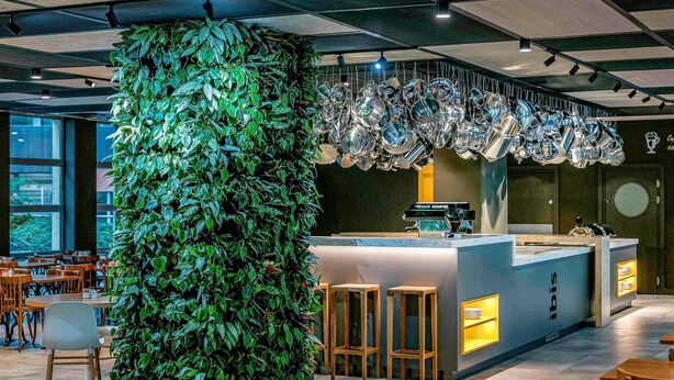 Un interior moderno con un jardín vertical verde, una zona de bar con taburetes y un área de estar con mesas y sillas.