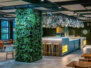 Un interno moderno con un giardino verticale verde, una zona bar con sgabelli e un’area salotto con tavoli e sedie.