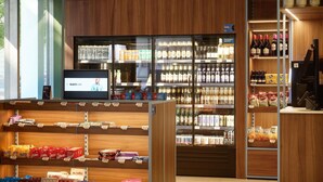 Interior de un supermercado con estantes llenos de snacks, una sección refrigerada con bebidas y una cámara de seguridad.