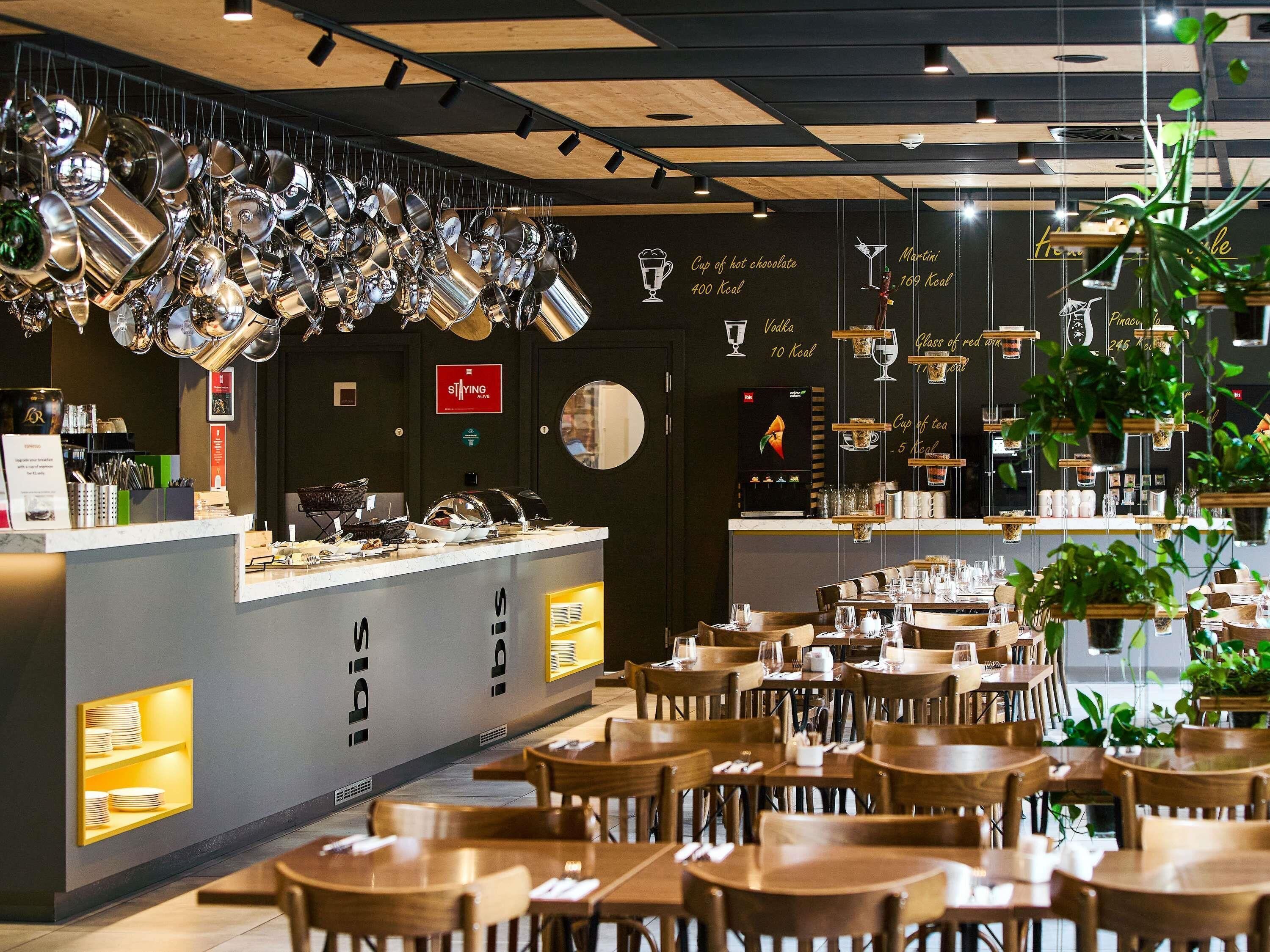 A modern cafe with a bar area, wooden tables, and hanging plants.