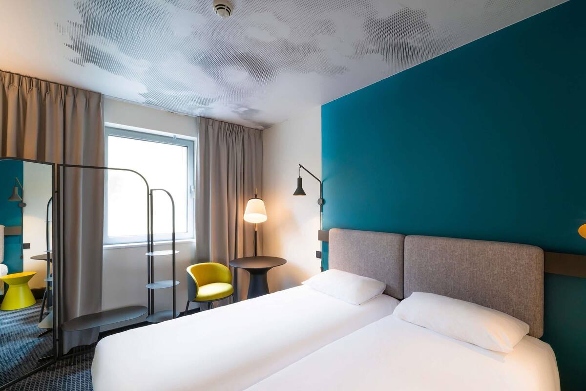A hotel room with a large bed, a desk, a chair, a lamp, and a window.