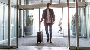 A man with a suitcase entering a building through a glass door. - ProfilHotels Mercur (Copenhagen)