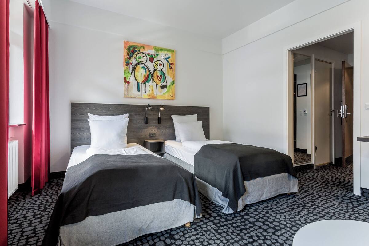 Una camera d'albergo con due letti, un quadro appeso al muro e un tappeto decorato.