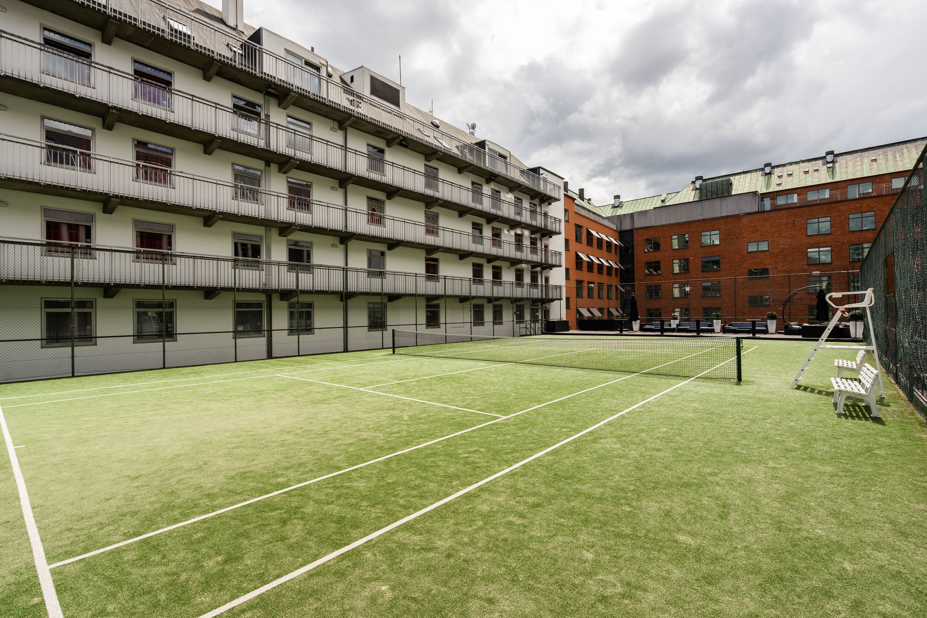 En tennisbana med nät, omgiven av höga byggnader med balkonger.