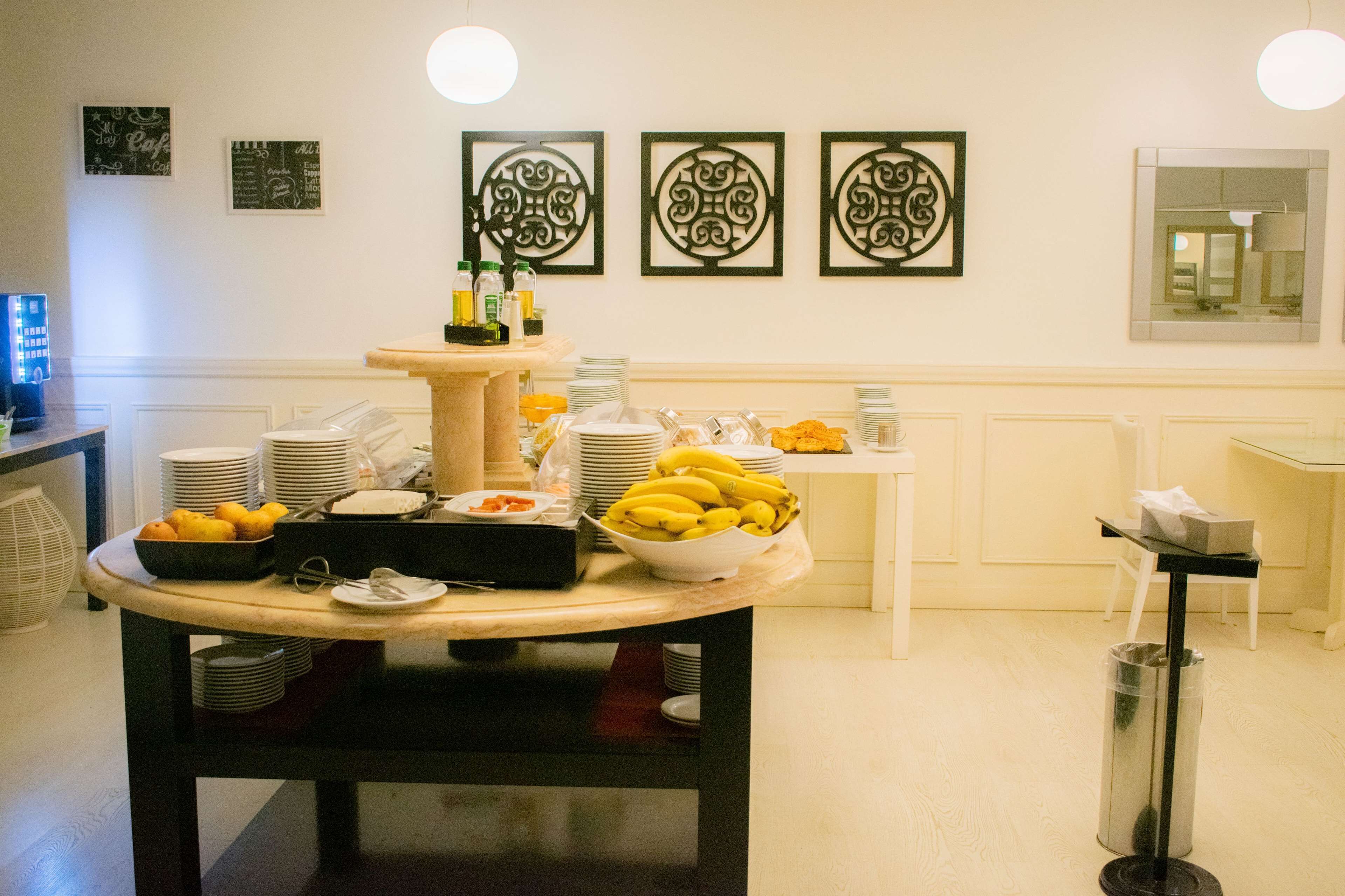A buffet setup with various food items and condiments, including bananas and lemons, arranged on a table with stacked plates and bowls.