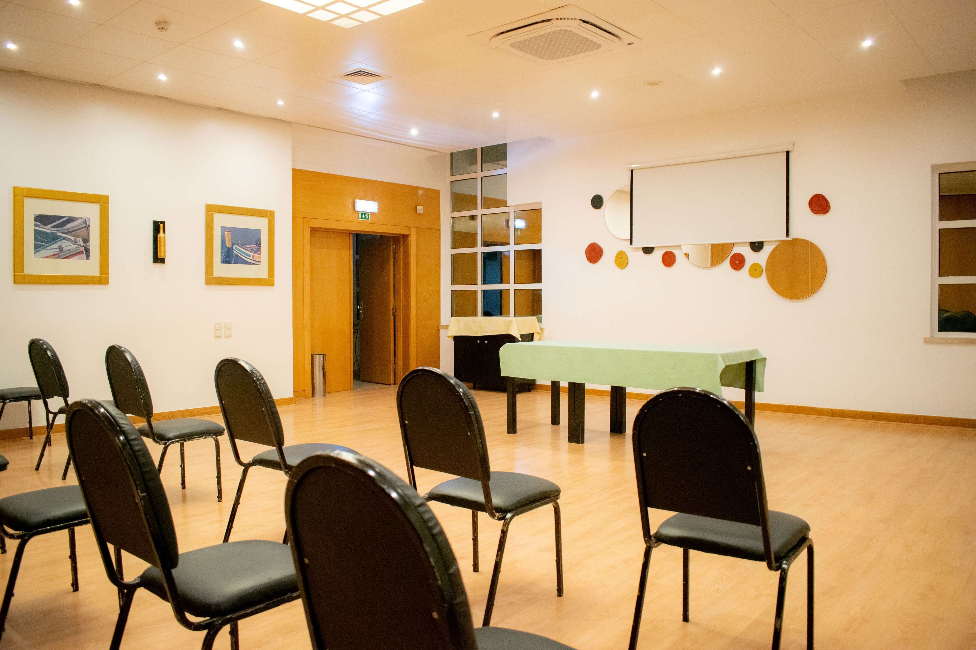 Uma sala de conferências com uma mesa comprida, várias cadeiras, obras de arte emolduradas nas paredes e uma janela com persianas.