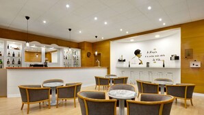 Un espace bar moderne avec des tables et des chaises rondes, un comptoir avec des bouteilles et un mur orné d’une citation.