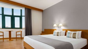 Une chambre d’hôtel avec un grand lit, deux lampes de chevet, une vue dégagée grâce à de grandes fenêtres du sol au plafond, une petite table et deux chaises.