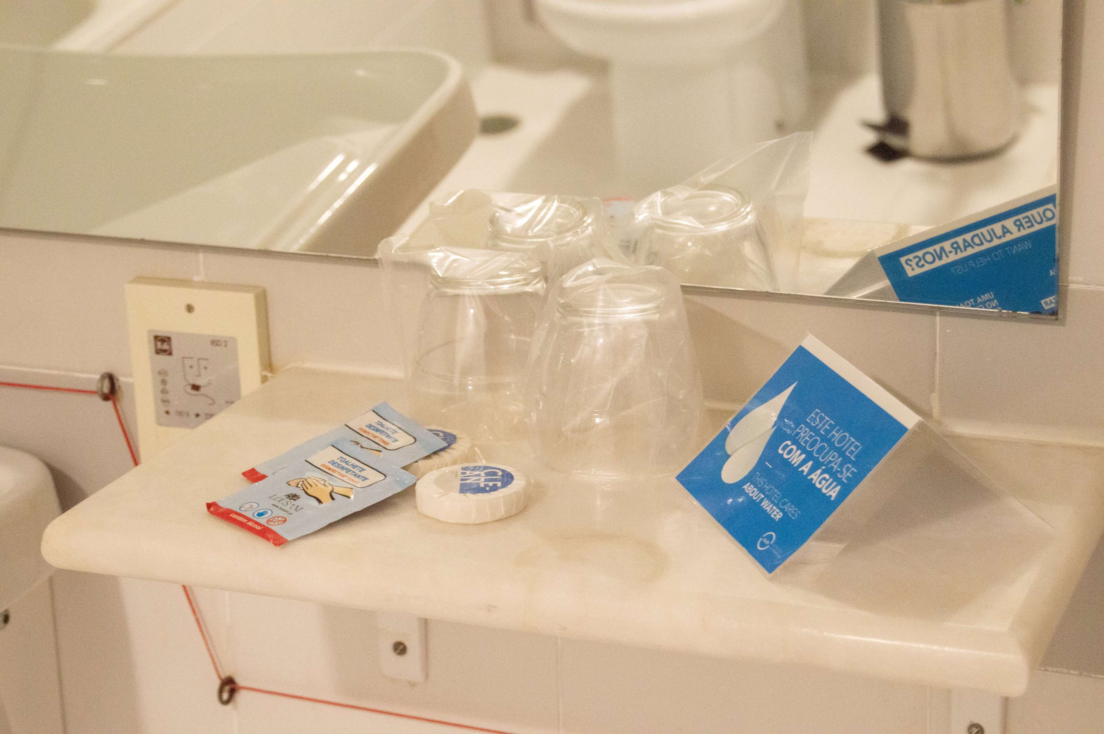A bathroom counter with toiletries, a mirror, and a sign about water conservation.