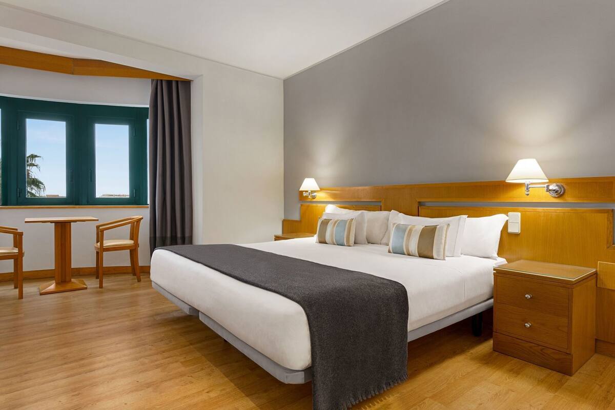 Una habitación de hotel con cama, mesitas de noche, un escritorio y sillas.