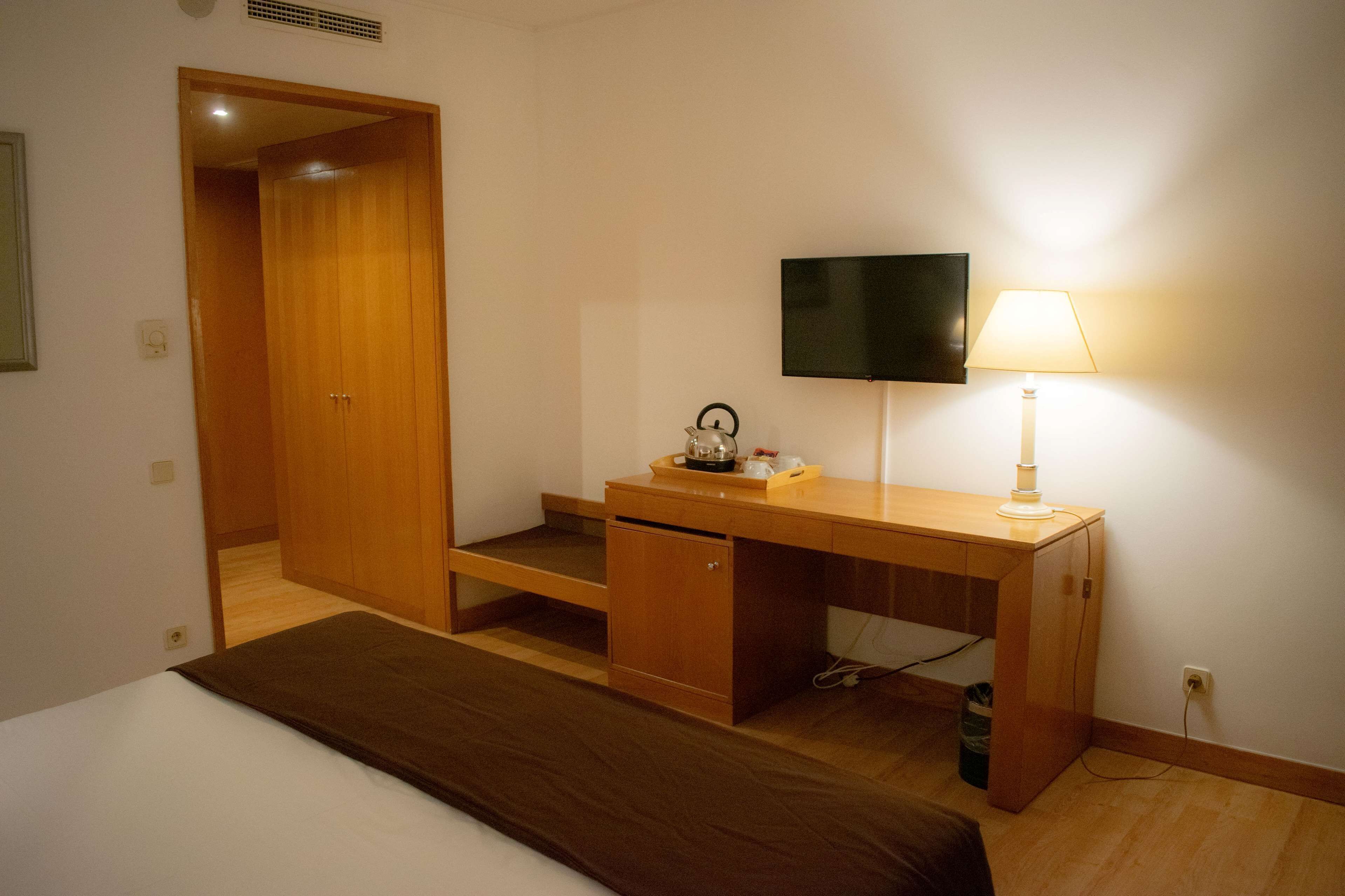 A hotel room with a wooden desk, a television, a lamp, and a bed.