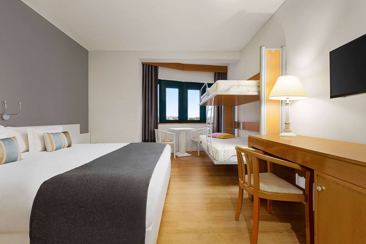 Habitación de hotel con cama, escritorio, silla y televisor.
