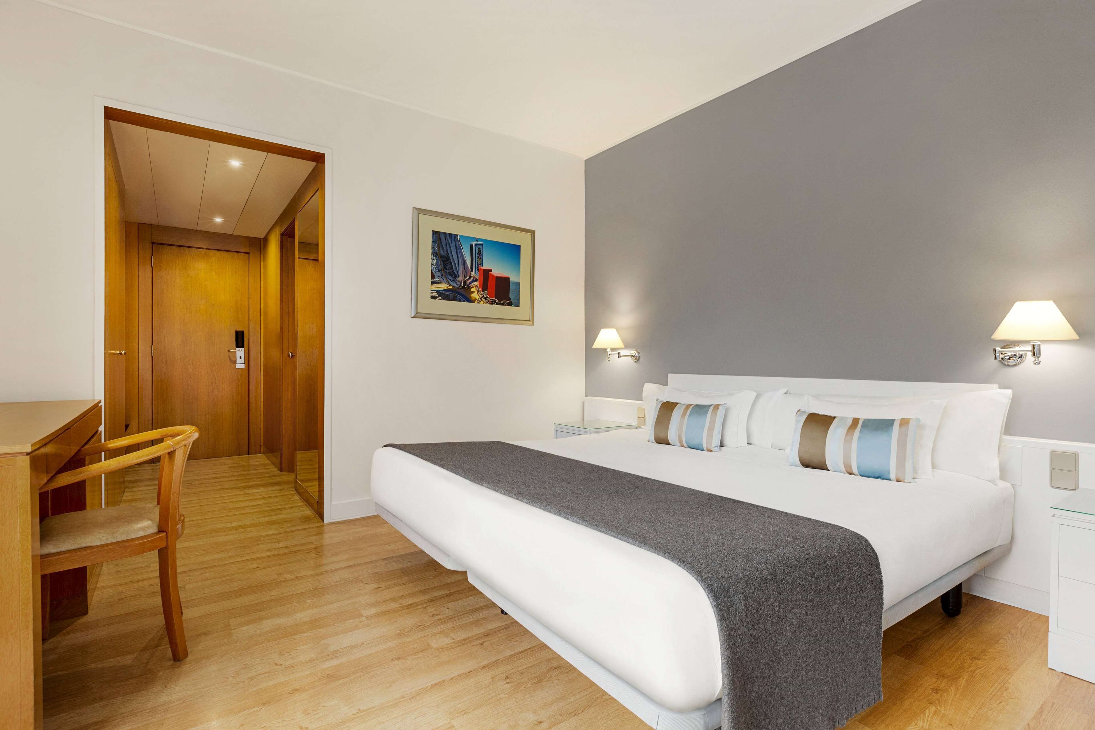 A hotel room with a bed, bedside lamps, a desk, and a chair.