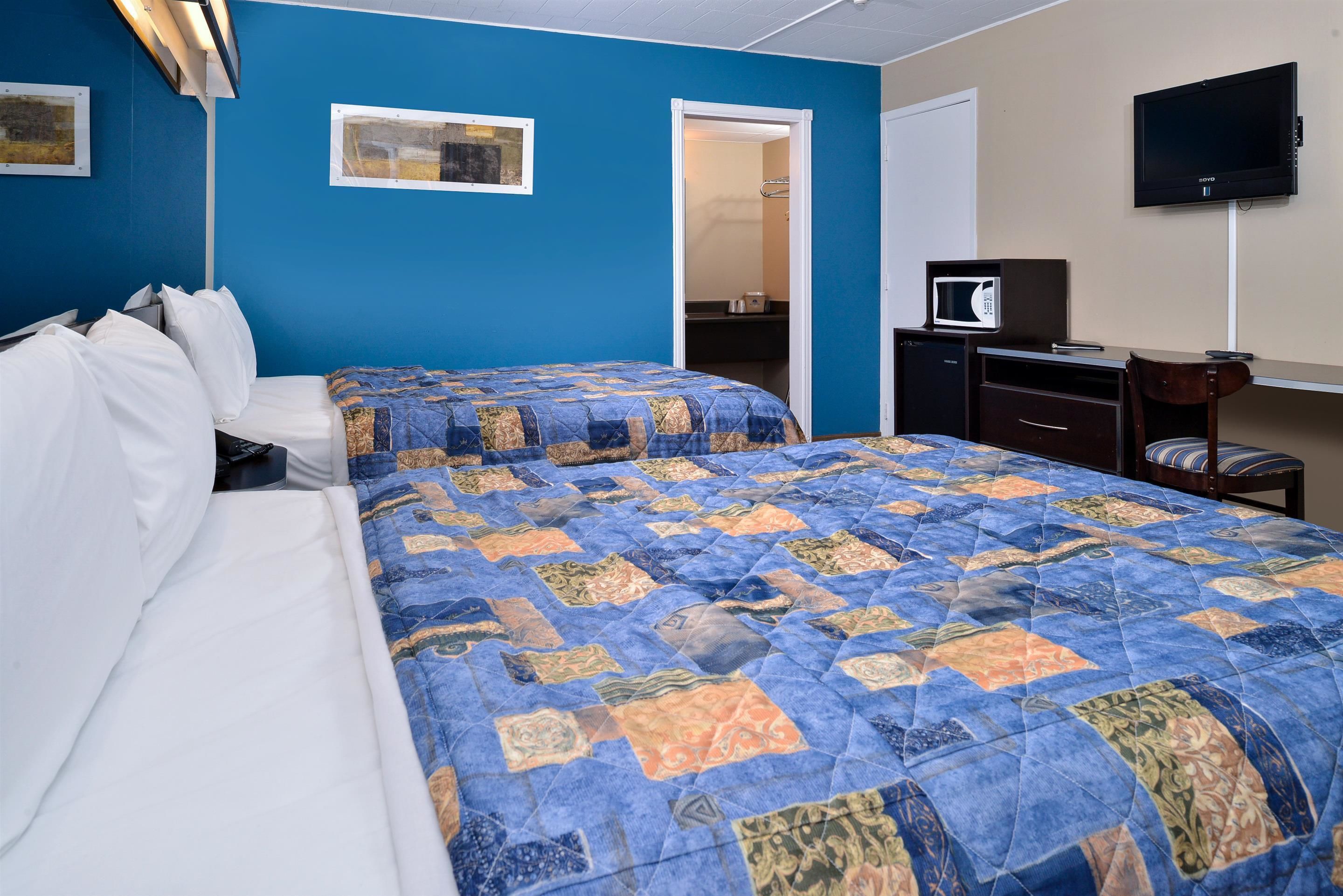 Ein Hotelzimmer mit zwei Betten, einem Schreibtisch mit Computer, einem Fernseher und einer Mikrowelle.