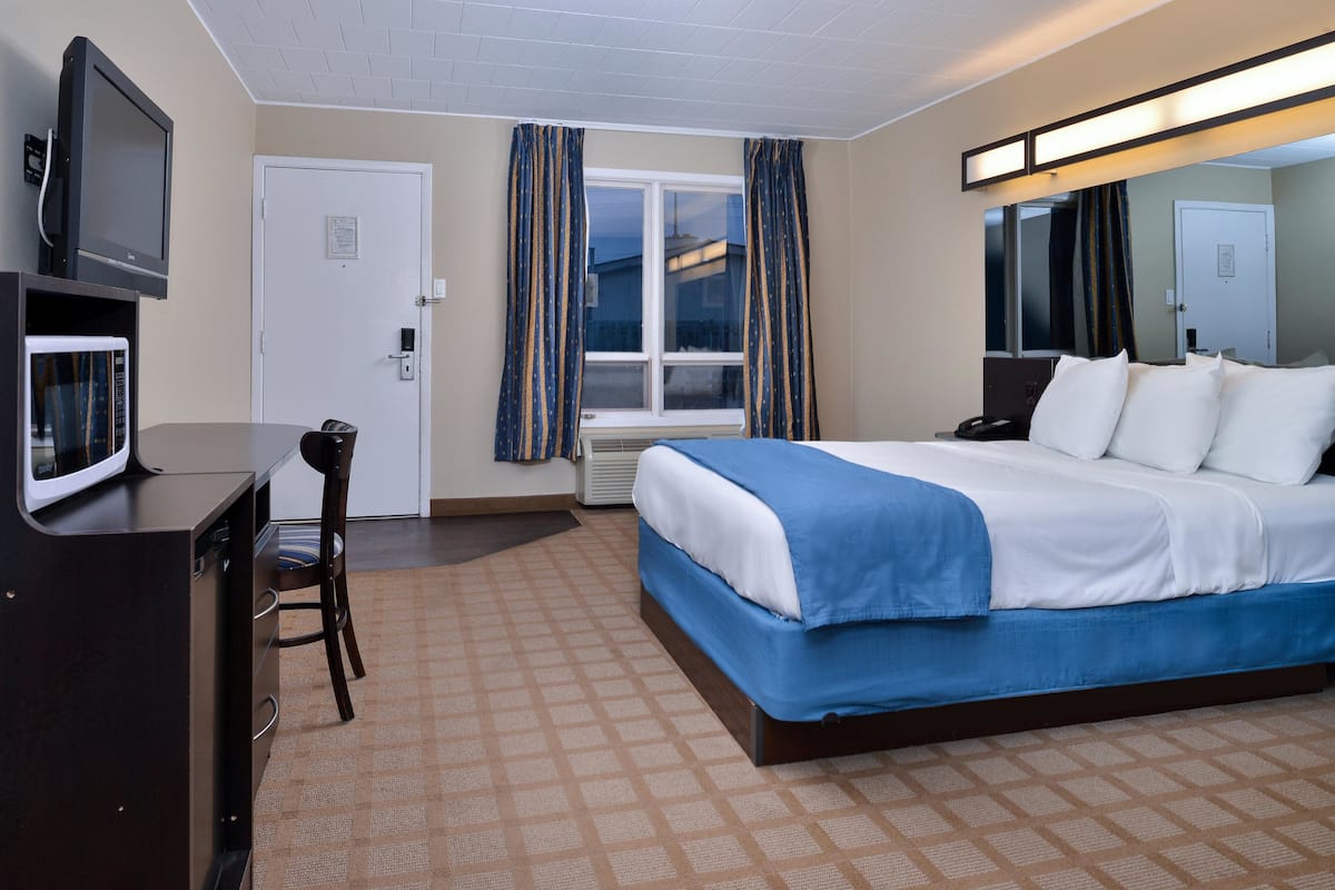 Habitación de hotel con cama, escritorio con televisor, silla, ventana con cortinas y espejo.