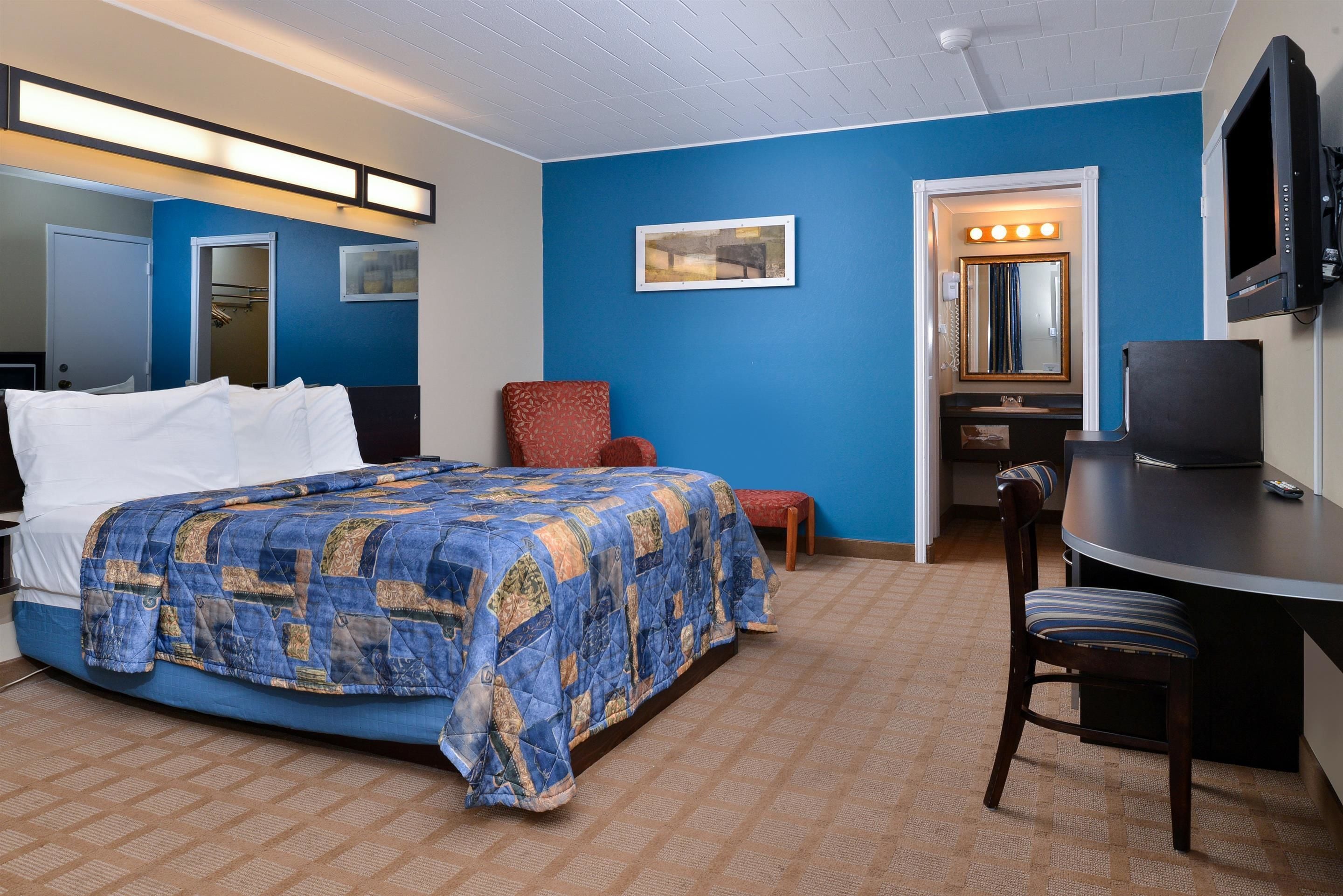 A hotel room with a bed, a desk, a chair, a mirror, and a television.