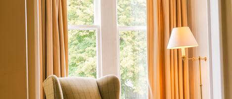 A chair in a room with a window, a lamp, and a small table.