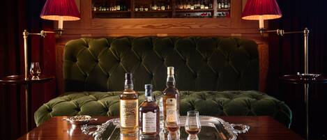 A bar area with a green tufted headboard, a tray with liquor bottles, glasses, and a silver tray.