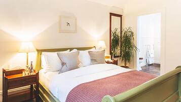 A hotel room with a bed, bedside tables, a nightstand, a mirror, a potted plant, and a door leading to a bathroom.