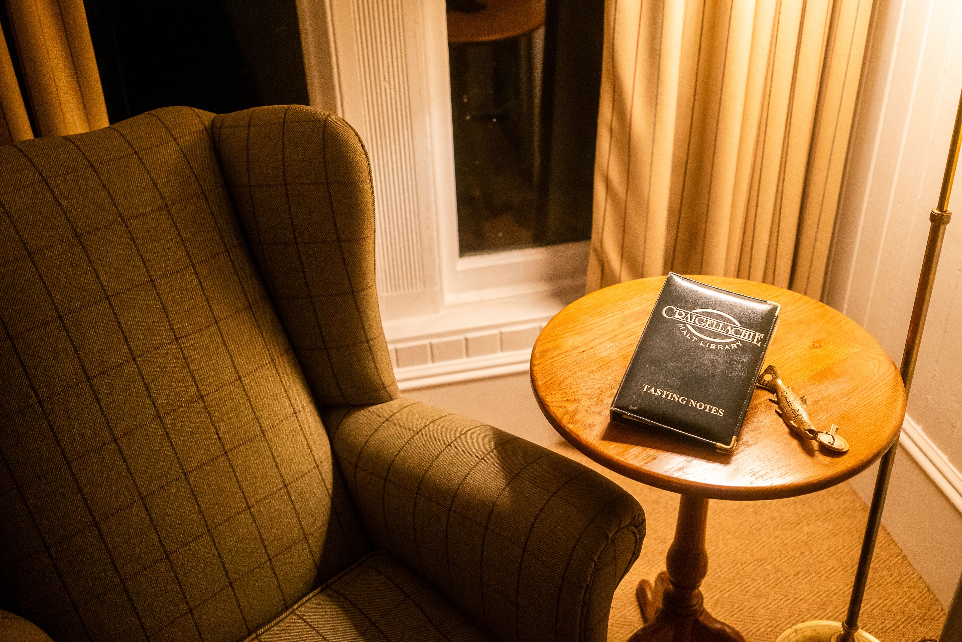 A room with a checkered armchair and a small wooden table with a book titled "Cellach" and a pen.