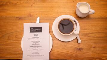 A wooden table with a menu, a cup of coffee, and a jug of milk.