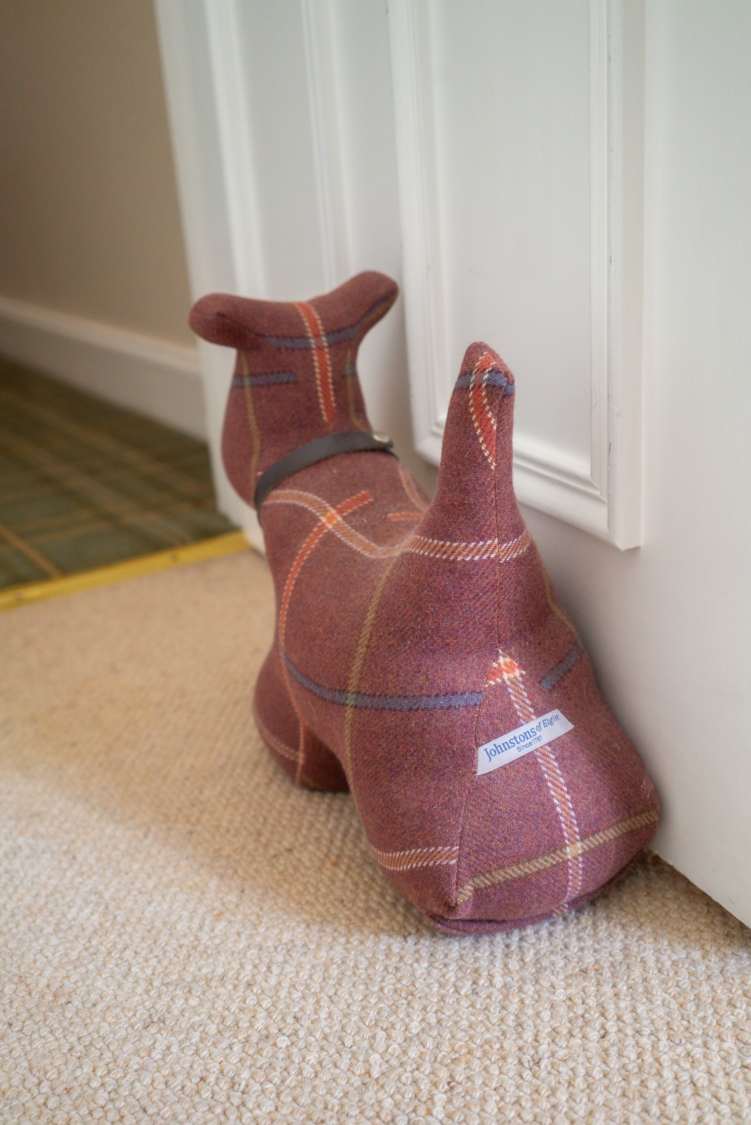 A plush toy resembling a dog on a beige carpet near a white door.
