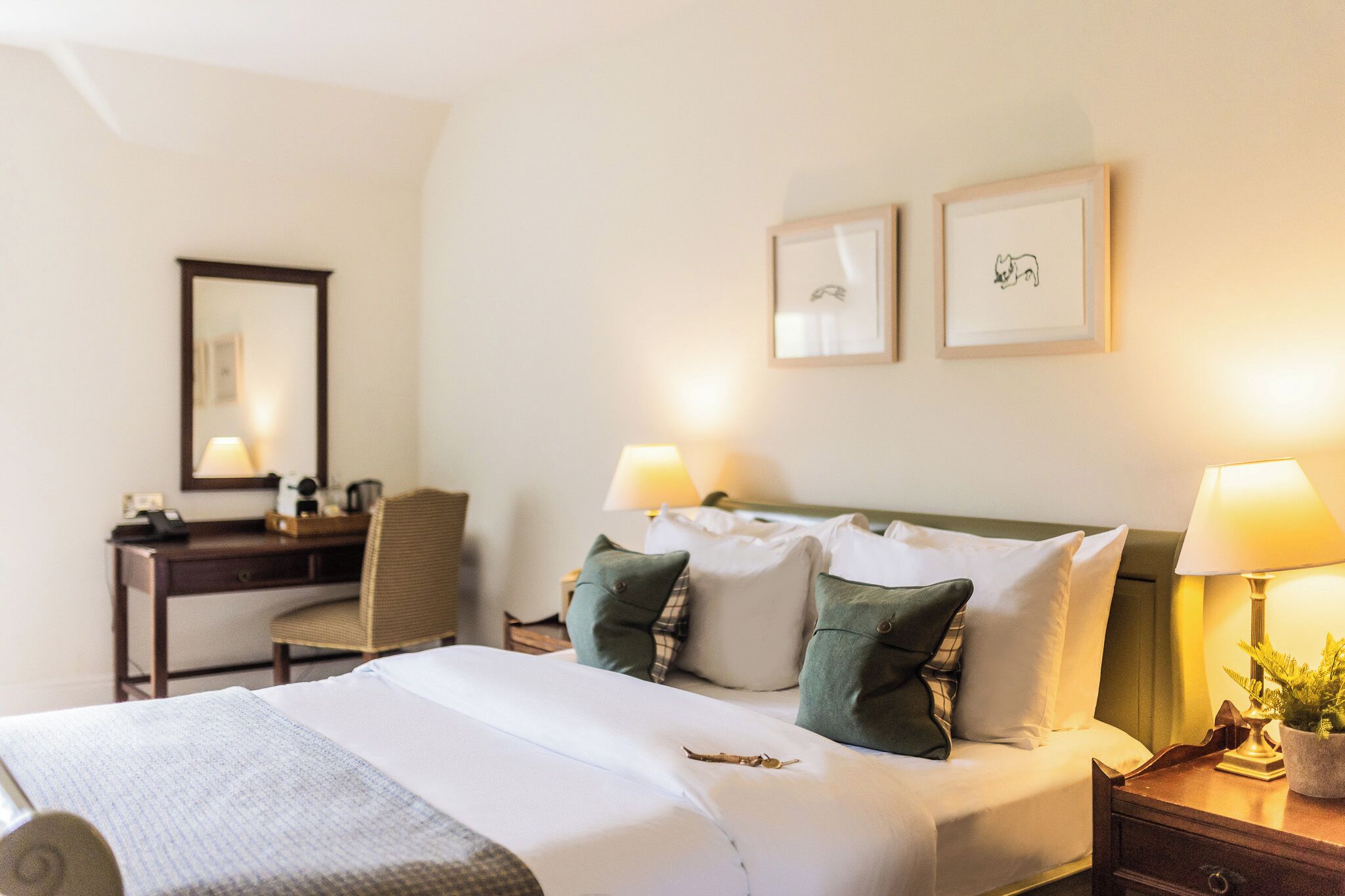 Una habitación de hotel con cama, dos lámparas de noche, un escritorio con silla y un espejo.