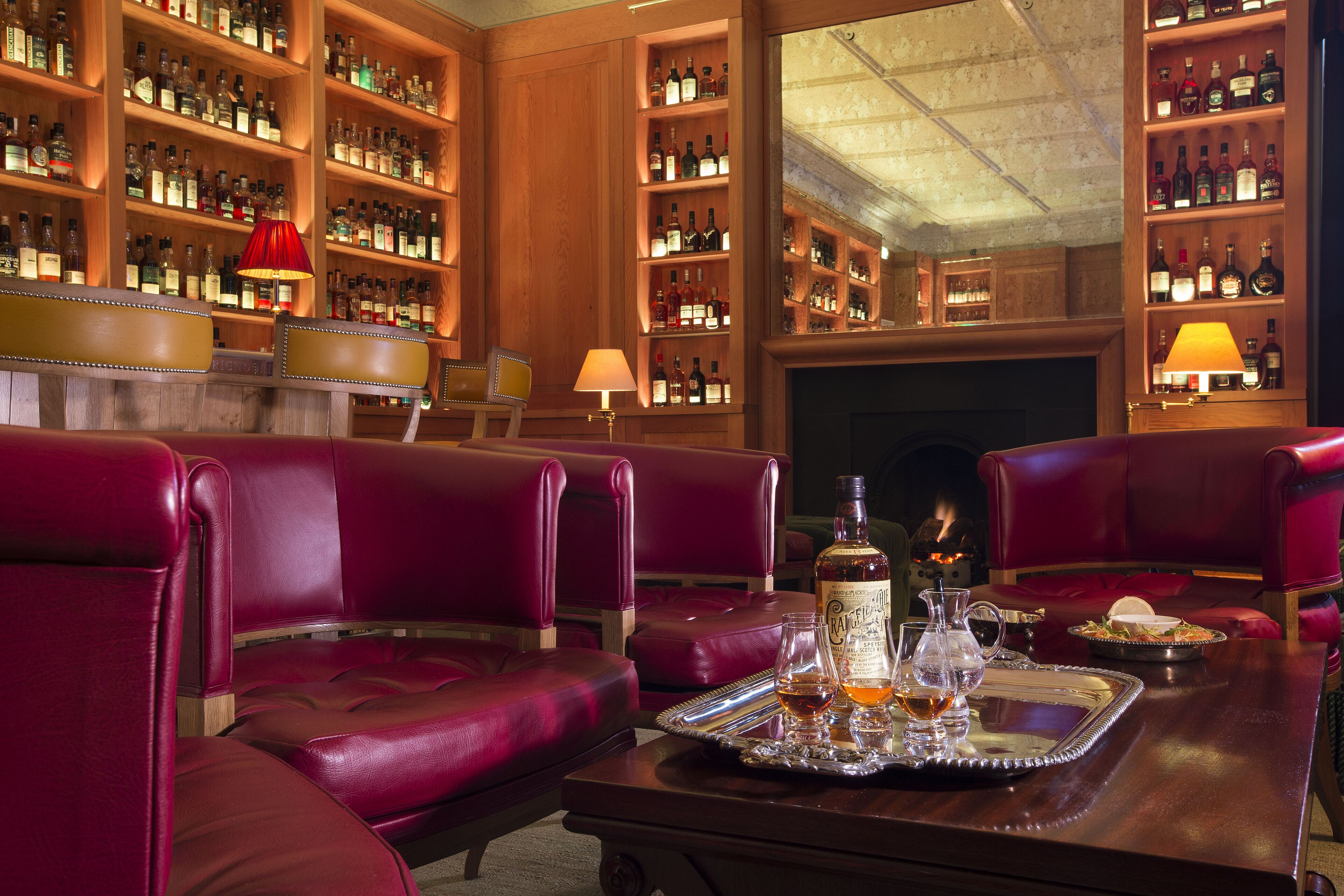 A bar area with leather seating, a tray with drinks, and shelves of liquor bottles.