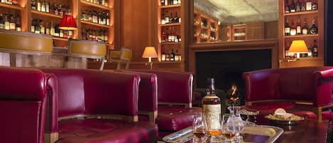 A bar area with leather seating, a tray with drinks, and shelves of liquor bottles.