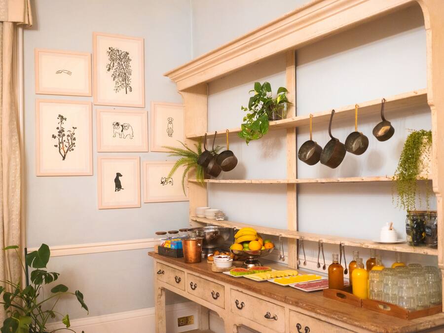 A kitchen with wooden shelves, framed botanical prints, and various kitchen utensils.