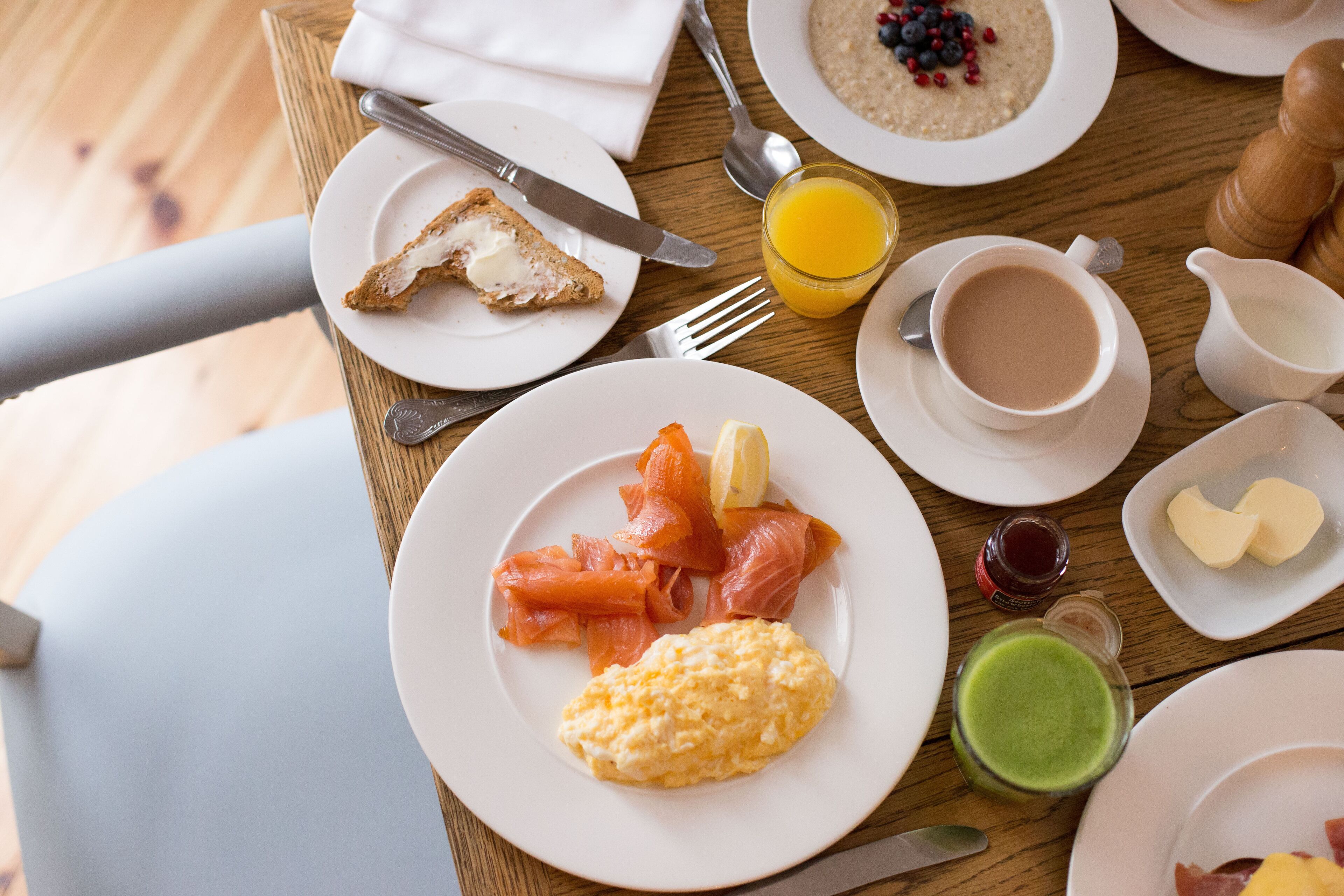 Una mesa de desayuno con platos de huevos, salmón ahumado, tostadas y un vaso de jugo de naranja.