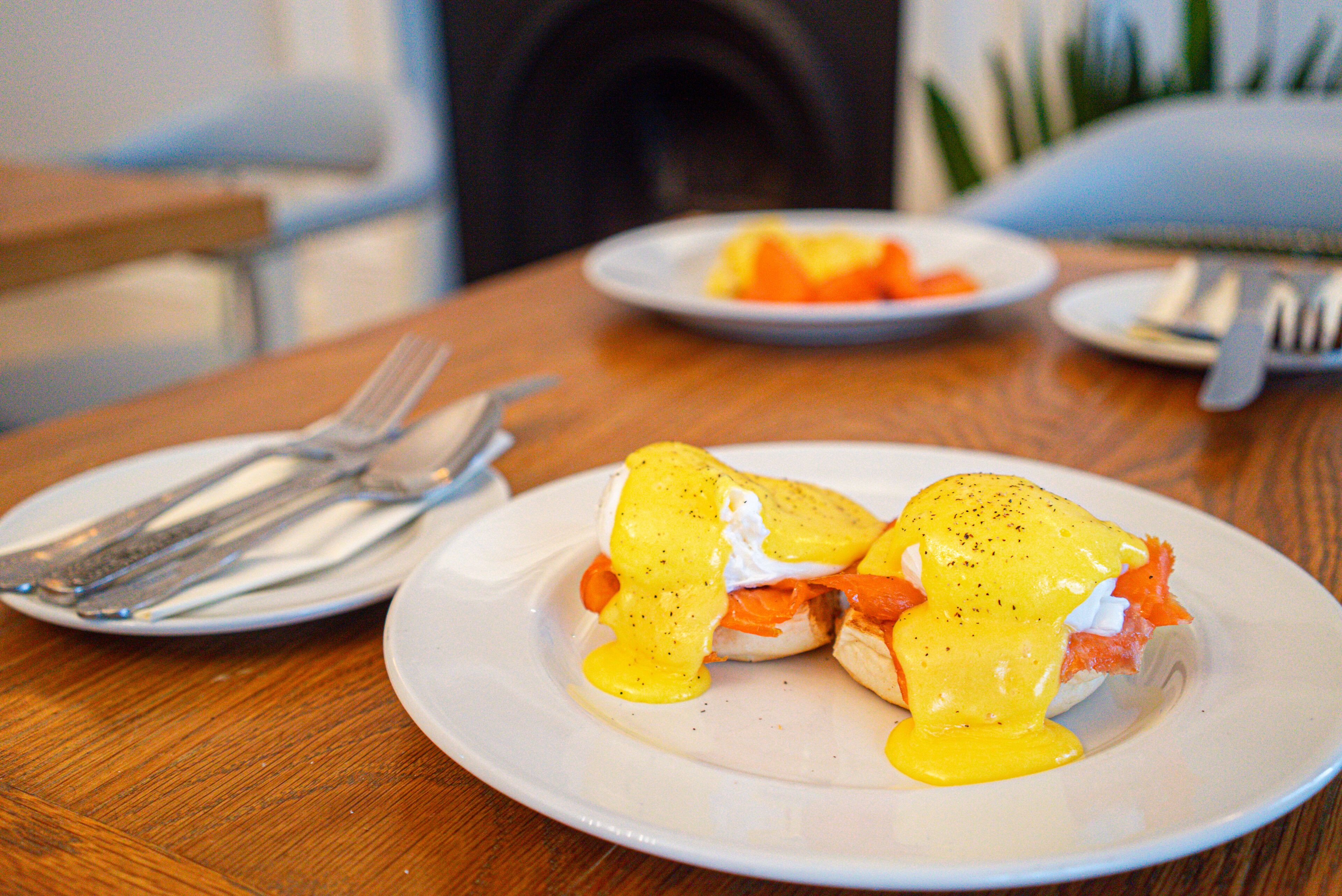 A dining table with plates of food, including eggs benedict and a plate of fruit.