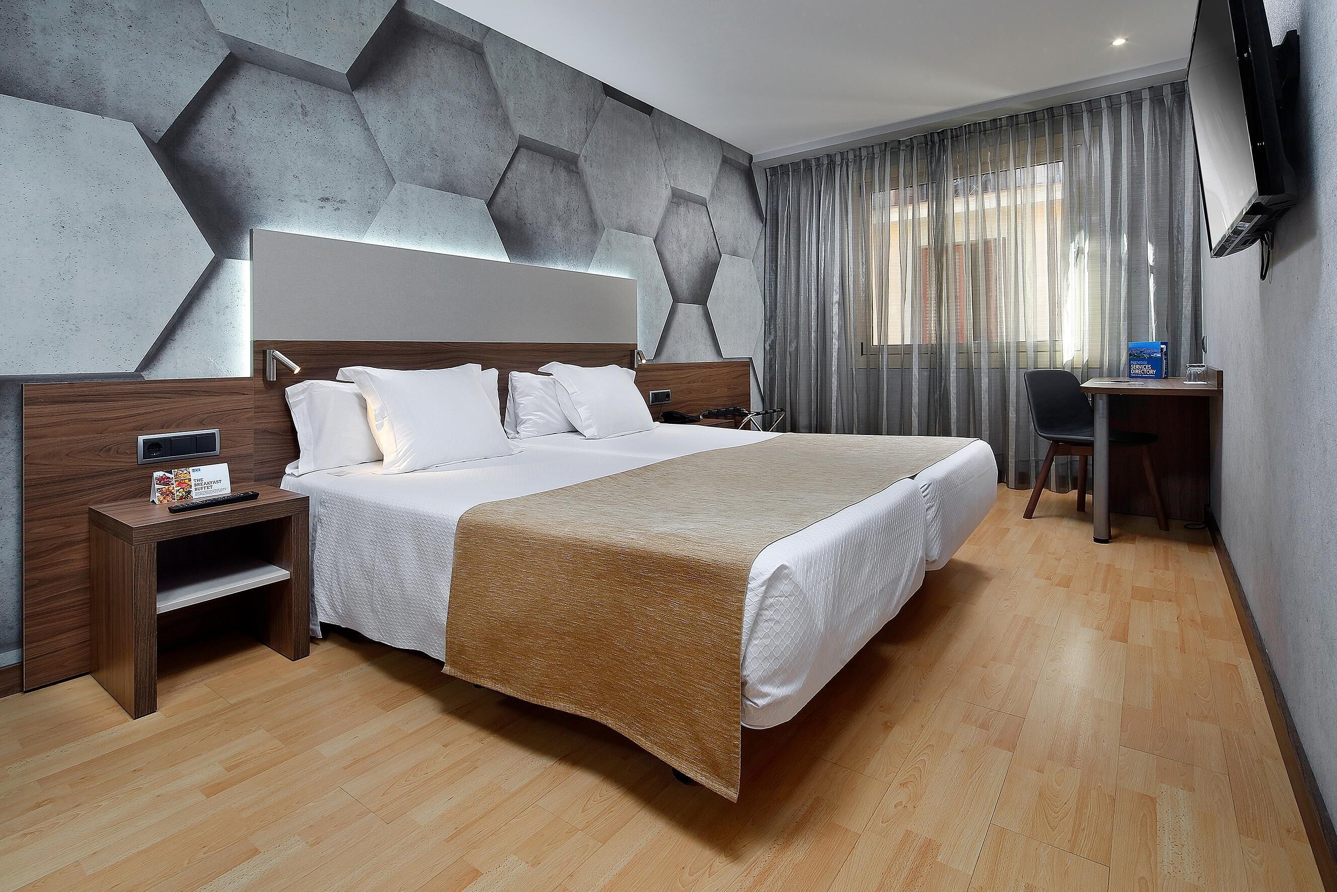 A modern hotel room with a large bed, wooden nightstands, a desk, and a TV.
