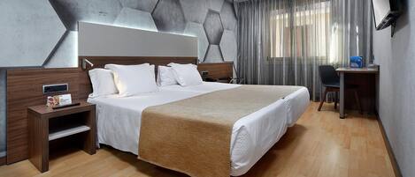 A modern hotel room with a large bed, wooden nightstands, a desk, and a TV.